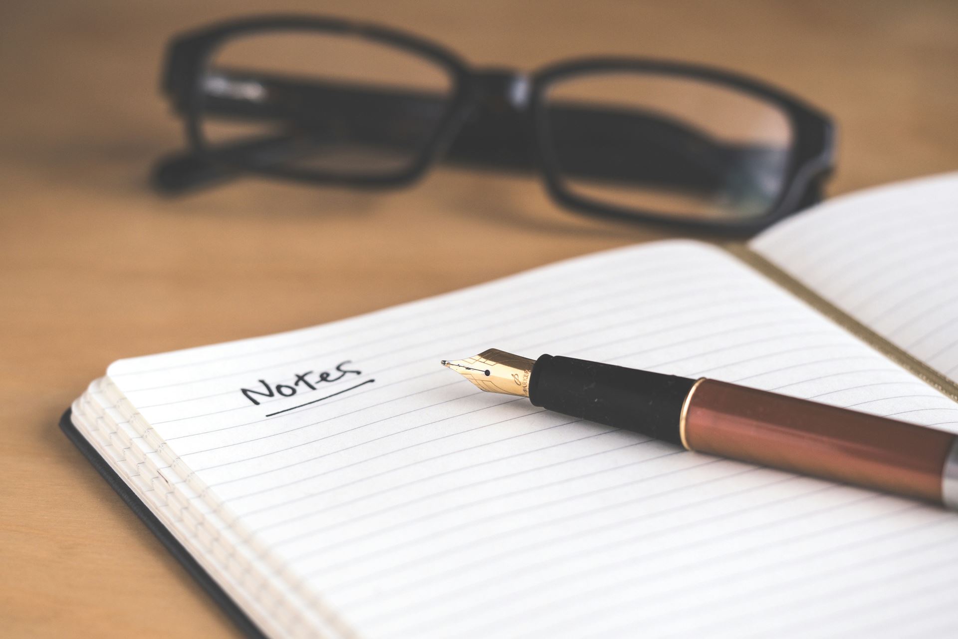 Notebook and pen with glasses in the background